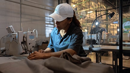 A UniFirst production Team Partner wearing a Micro Piqué Polo Shirt and baseball with the UniFirst logo repairs garments as part of the gurantee that comes with a UniFirst uniform rental program.