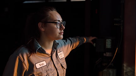A shop technician wearing UniWear® Cotton Blend Zip Front Shop Coveralls personalized and laundered by UniFirst looks out at the sunrise.