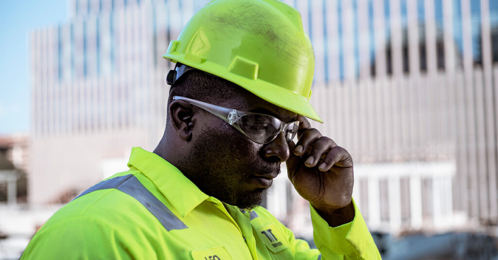 Construction worker wearing hard hat, safety glass, and high visibility uniform shirt at a work site.