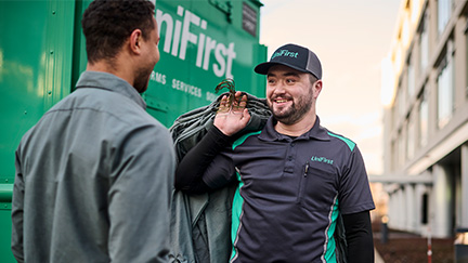 UniFirst RSR standing with customer holding uniforms explaining how to take their uniform service to the next level