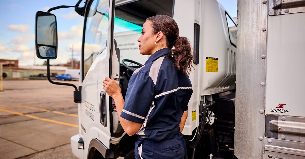Truck driver wearing a UniFirst uniform shirt with enhanced visibility opening the door of a truck.