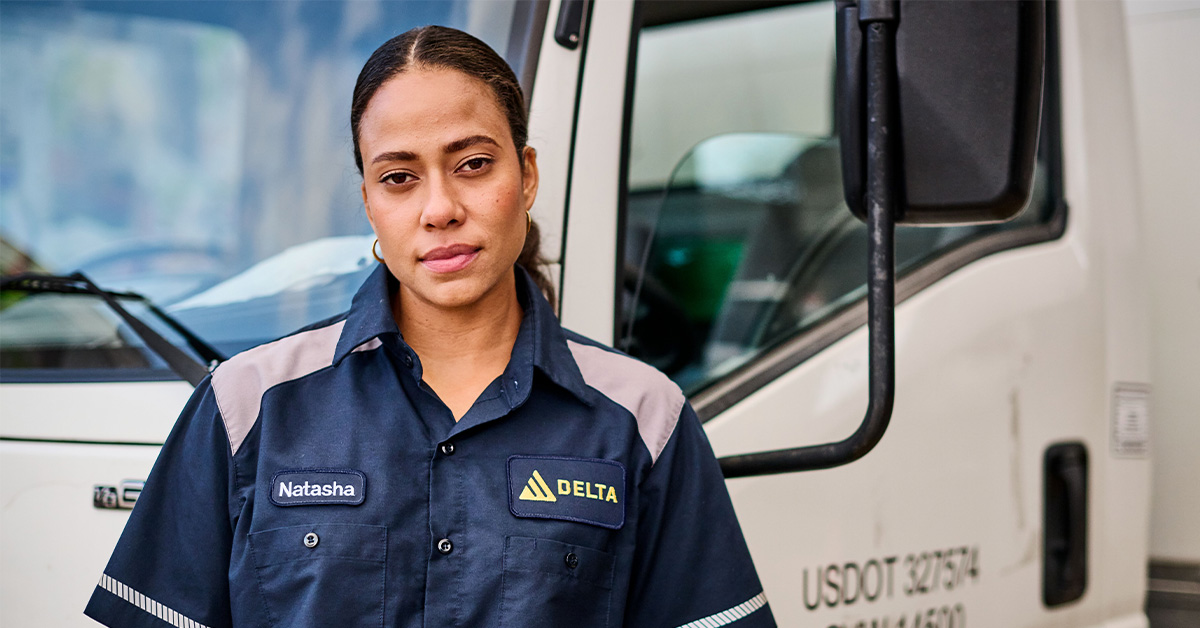 Woman working in the transportation and warehousing industry standing in front of a truck wearing UniFirst workwear