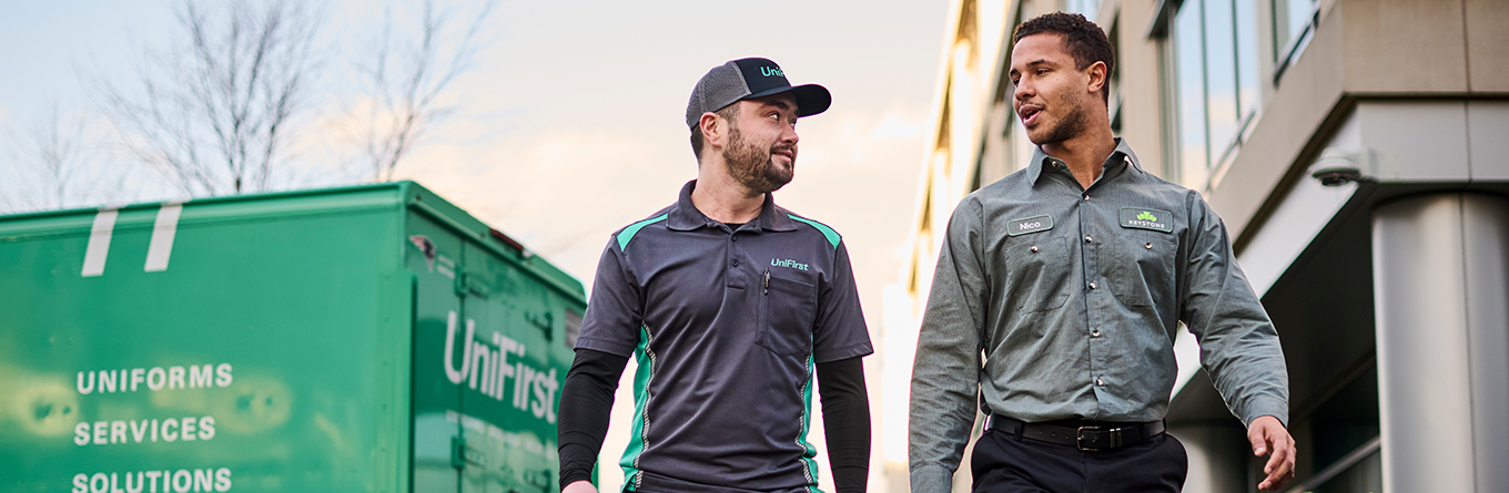 A UniFirst expert with a business owner, showcasing clean, branded work uniforms and a UniFirst service truck in the background.