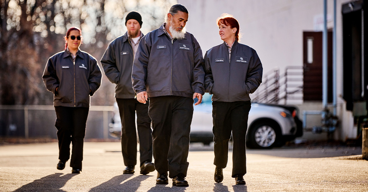 Group of workers wearing UniFirst work pants walking in a parking lot.