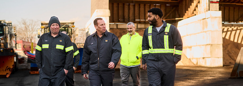 A group of workers walking and chatting in an industrial work environment wearing UniFirst uniforms
