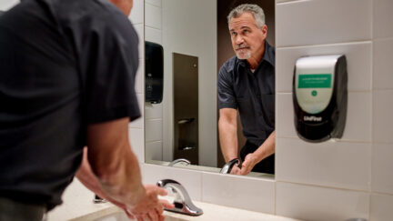 Worker washing hands using commercial hand soap in a public restroom with paper towels