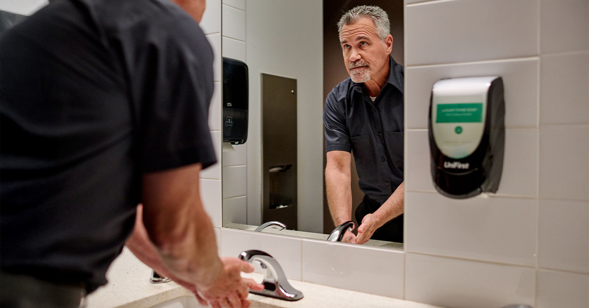 Worker washing hands using commercial hand soap in a public restroom with paper towels