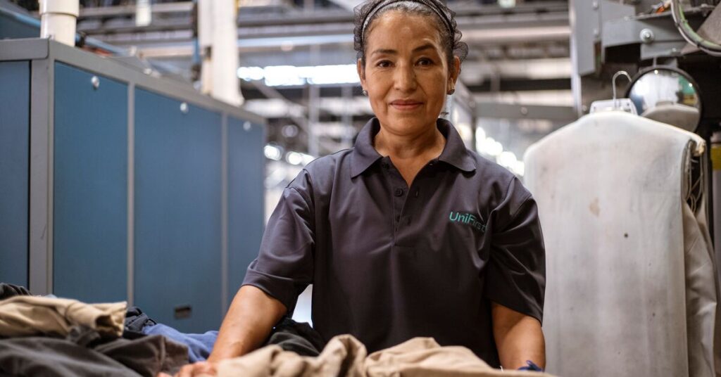 A women stands smiling in a plant that industrial launders uniforms