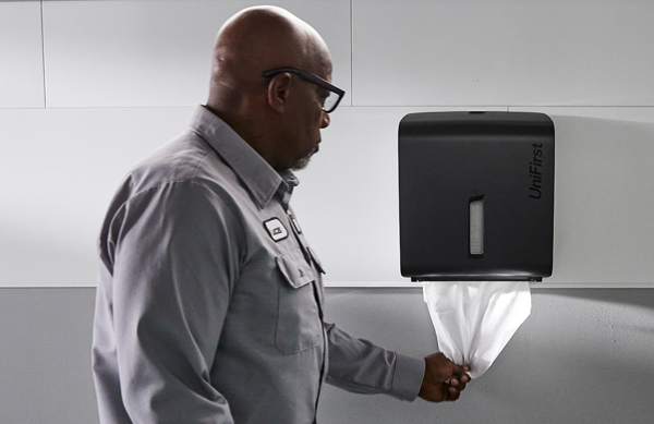 A man using an Essential Series Paper Towel Roll Dispenser in a commercial restroom