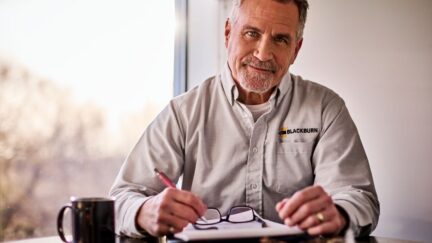 A man sitting at a table smiling while wearing a UniFirst uniform knowing his procurement strategy is in control.