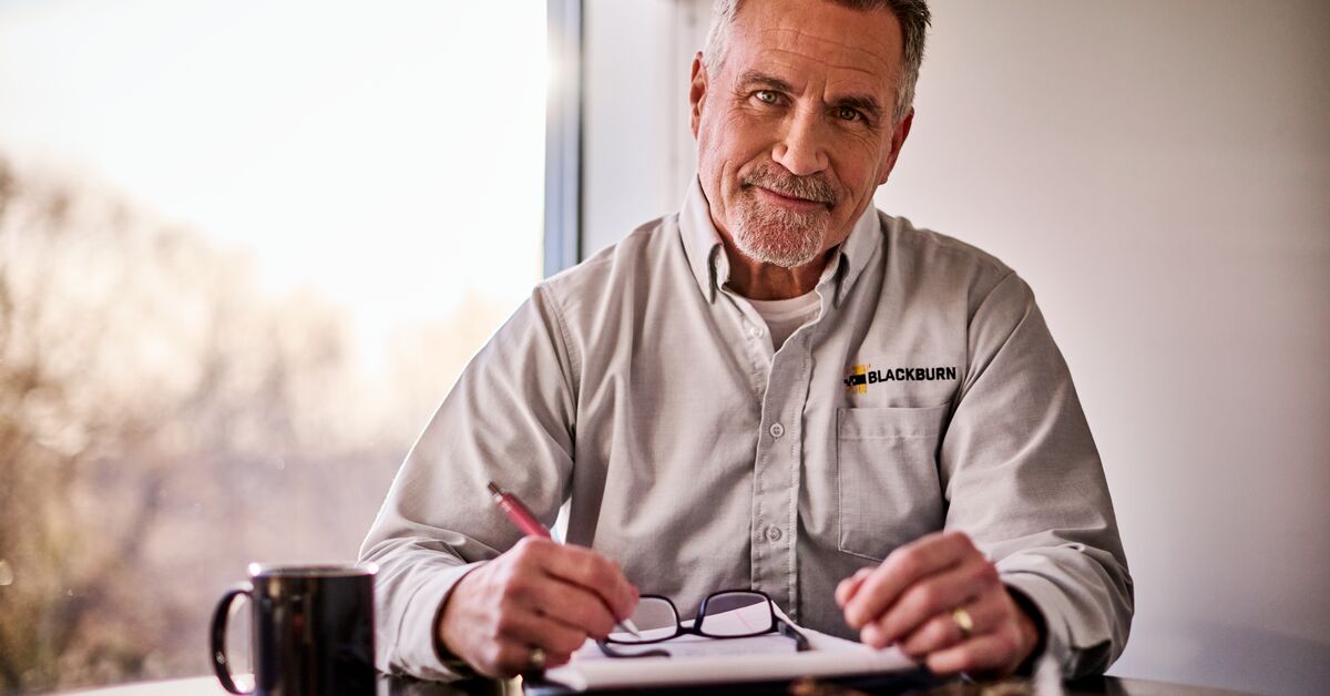A man sitting at a table smiling while wearing a UniFirst uniform knowing his procurement strategy is in control.