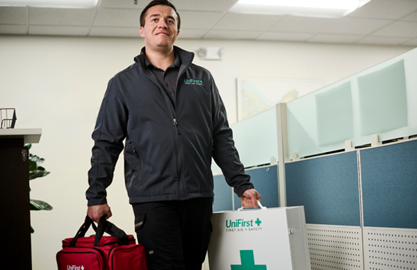 A UniFirst representative carrying a UniFirst First Aid + Safety first aid kit