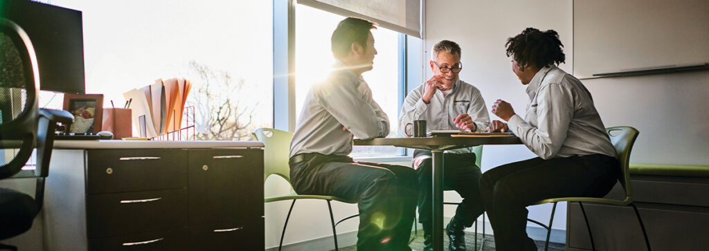 Three people sitting at a table wearing professional looking uniforms while chatting at work