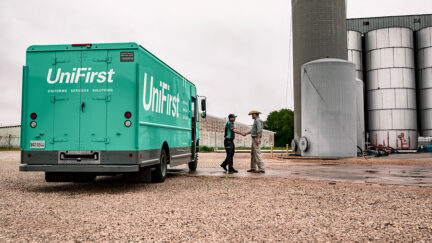 UniFirst truck pictured with RSR delivering uniforms and facility service products, and shaking hands with a customer.