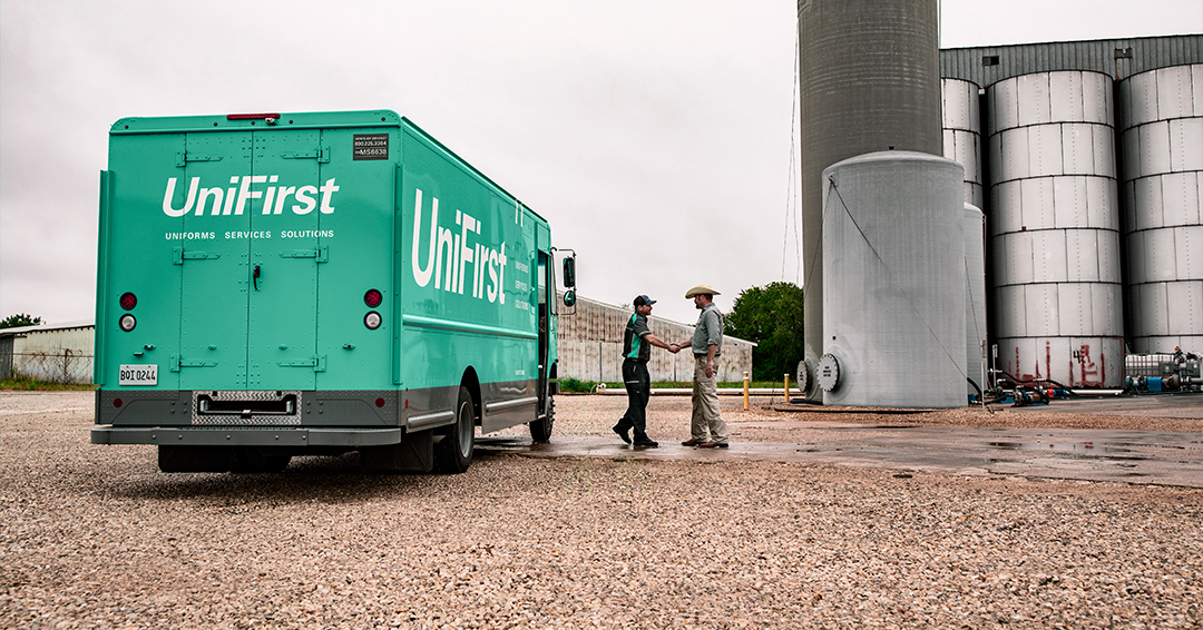 UniFirst truck pictured with RSR delivering uniforms and facility service products, and shaking hands with a customer.