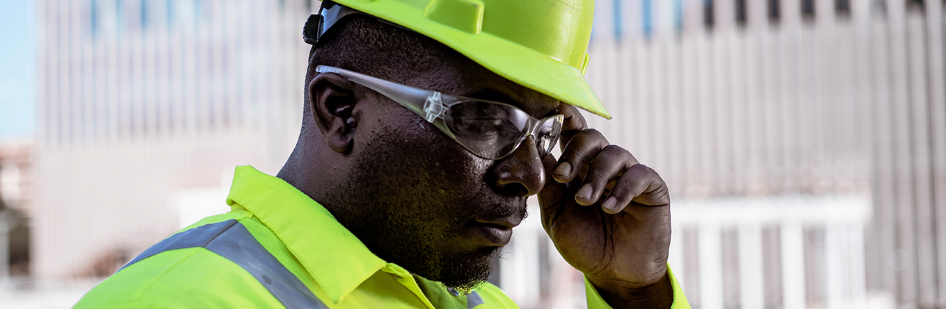 A worker adjusts his safety glasses while wearing a high visibility uniform in a construction area