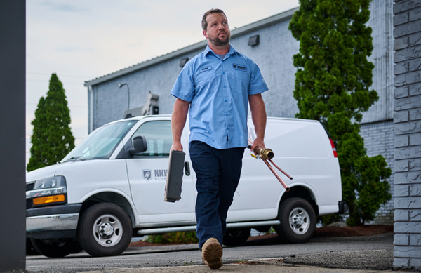 A plumber walking out of a work truck smiling with his uniform program workwear