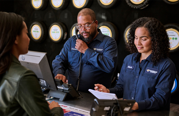 Two retail workers at a counter helping customers while wearing employee uniforms