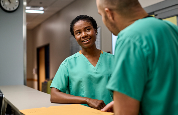 Two healthcare workers in conversation while wearing scrubs as part of a uniform program