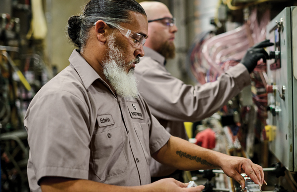 Two workers in manufacturing do their job while wearing employee uniforms