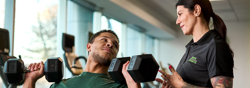 A personal trainer working with a client in a gym while wearing a work uniform