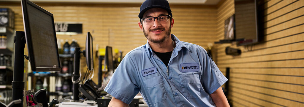 A retail worker standing at a computer smiling while wearing his employee uniform