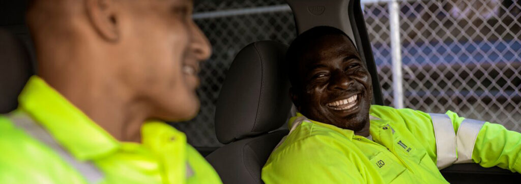 Two men sitting in a truck laughing while wearing high visibility clothing for jobsite safety