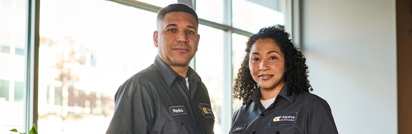 A man and a woman stand together at work while wearing UniFirst work shirts as part of a rental program