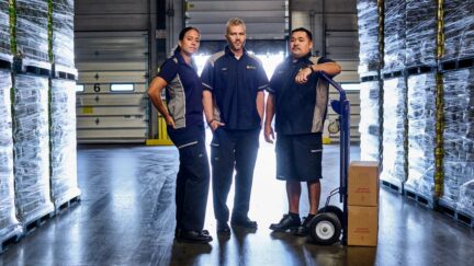 Three employees standing in a warehouse wearing their employee uniforms