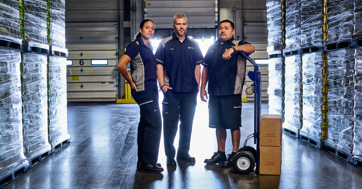 Three employees standing in a warehouse wearing their employee uniforms