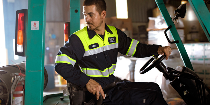 A worker operating a forklift wearing high visibility clothing in a warehouse setting