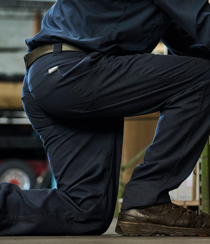 A worker kneeling in a warehouse wearing comfortable workwear pants that stretch