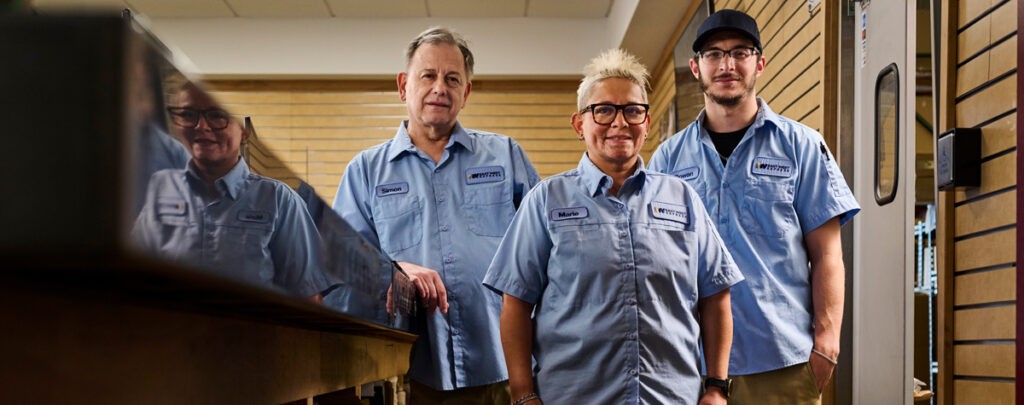 A team of active workers standing behind the counter of a business wearing Always U work uniforms in light blue and khaki