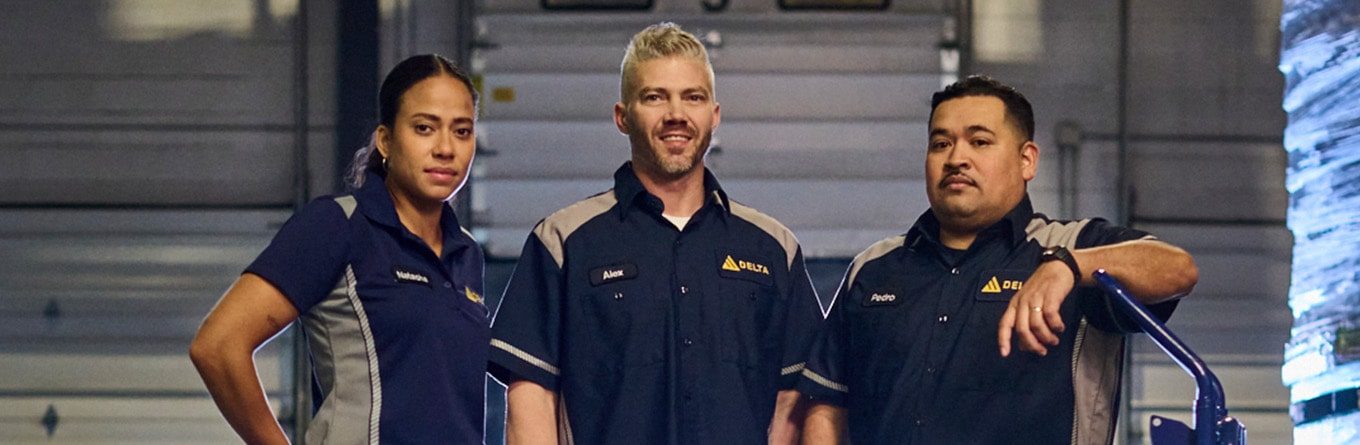 Three employees of a packaging and logistics company wear navy blue and grey Spotlite MV work shirts and polo shirts as part of a custom uniform program provided by UniFirst.